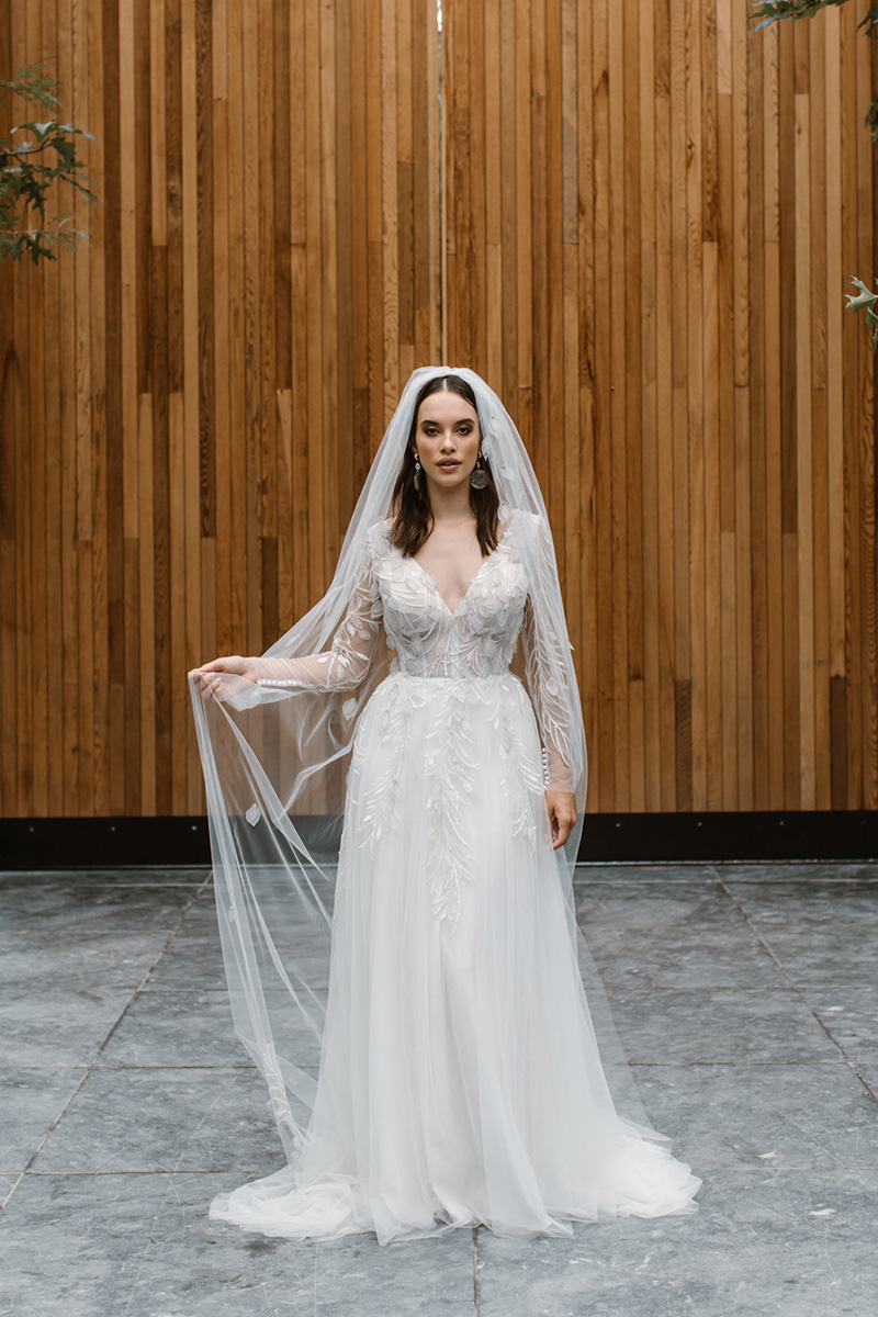 A soft A-line wedding dress scattered in a unique leaf lace and sheer long sleeves is designed for the ultra-romantic bride with a bit of a wild side.